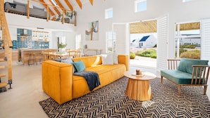 A spacious loft with a high ceiling, a kitchen area, a living room with a yellow sofa, and large windows. - Waterbird Coastal Retreat (Velddrif)