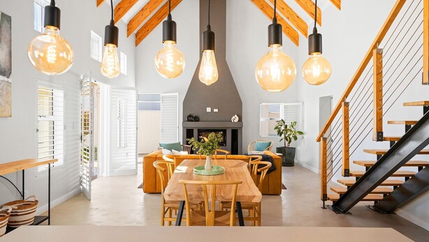 A modern interior with a wooden dining table, chairs, hanging light fixtures, and a staircase. - Waterbird Coastal Retreat (Velddrif)
