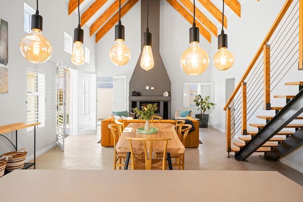 Un intérieur moderne comprenant un coin repas, un escalier en bois et des poutres apparentes.
