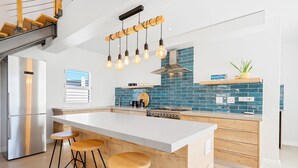 A modern kitchen with a central island, bar stools, a stainless steel refrigerator, and a blue-tiled backsplash. - Waterbird Coastal Retreat (Velddrif)