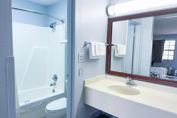 Un baño con bañera, inodoro, lavamanos y espejo con marco de madera.