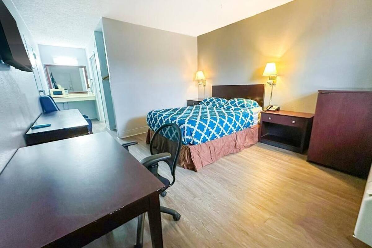 A hotel room with a bed, desk, chair, bedside tables, lamps, and a mirror.