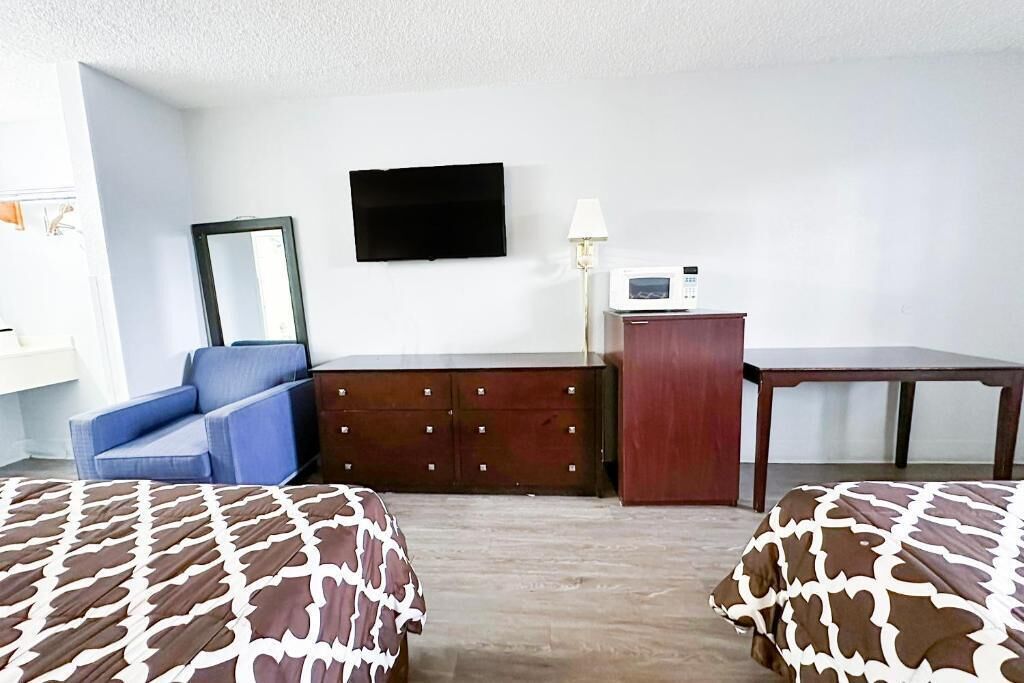 A hotel room with a bed, a dresser, a desk, a television, and a lamp.