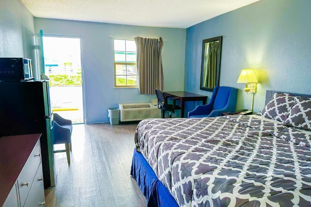 A hotel room with a bed, desk, chair, and a view of the outdoors.