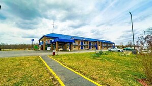 A motel with a blue roof, a parking lot, and a grassy area with a pathway. - Happy Extended stay (Madisonville)