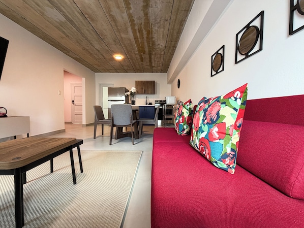 A modern living room with a red sofa, a wooden coffee table, and a kitchen area in the background.