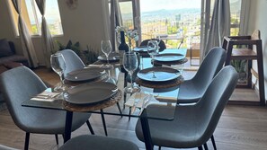 Een eettafel gedekt met borden, glazen en een fles, omringd door grijze stoelen in een kamer met grote ramen.