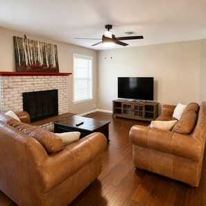 A living room with a fireplace, leather sofas, a TV, and a ceiling fan. - Spacious 3-bedroom house close to Texas Tech. Great neighborhood!! (Lubbock)