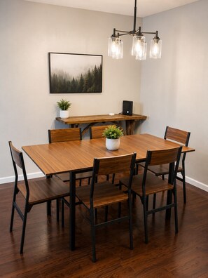 A dining area with a wooden table, six chairs, a chandelier, a framed picture on the wall, and a small plant on the table. - Spacious 3-bedroom house close to Texas Tech. Great neighborhood!! (Lubbock)