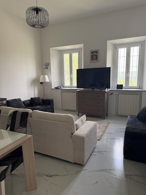 A living room with a sofa, a TV, a lamp, and a window with a view. - Cascina Moretta!!! It is a pleasure to have you here in the authentic heart of Monferrato. (Piemonte)