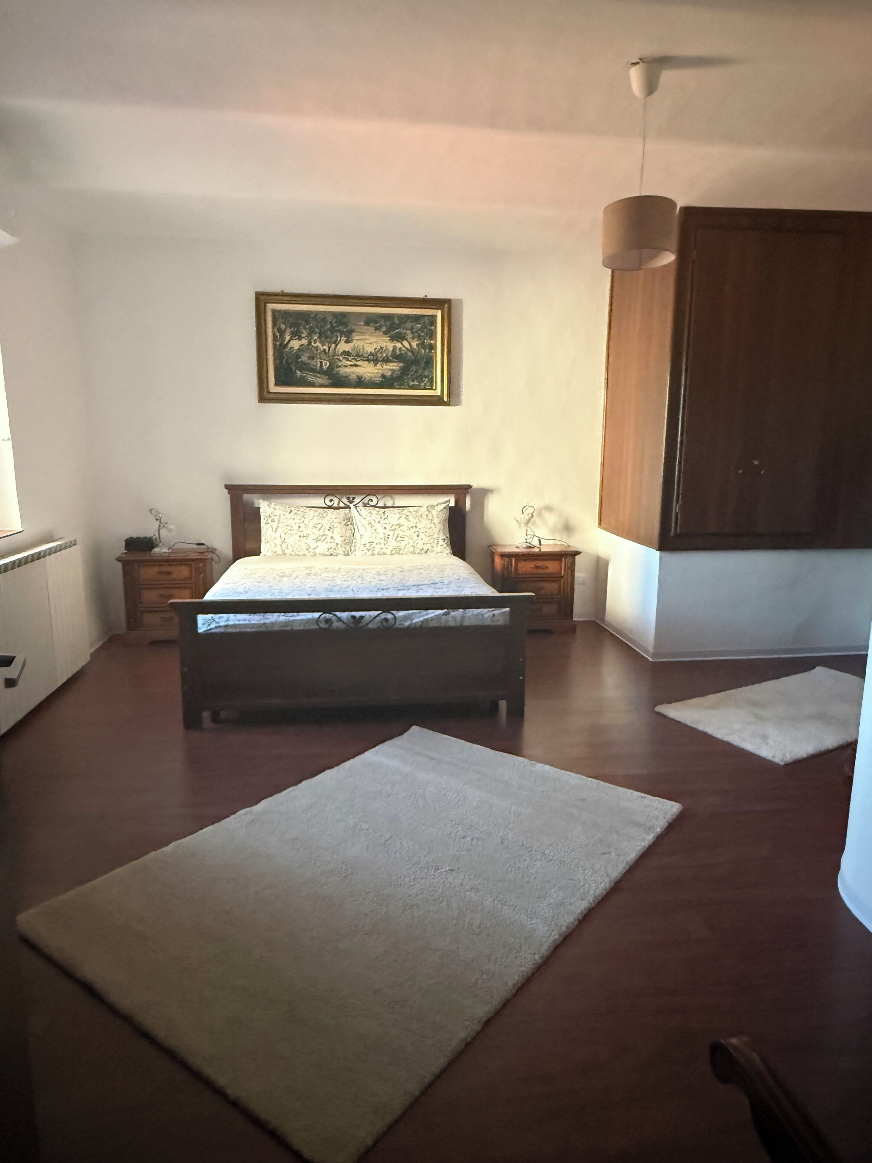 Ein Schlafzimmer mit Bett, Nachttisch, Schminktisch, einem Bild an der Wand und einem großen Teppich.