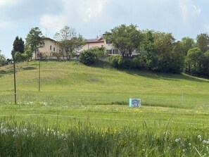A rural landscape with a house on a hill, surrounded by greenery and a field. - Cascina Moretta!!! It is a pleasure to have you here in the authentic heart of Monferrato. (Piemonte)