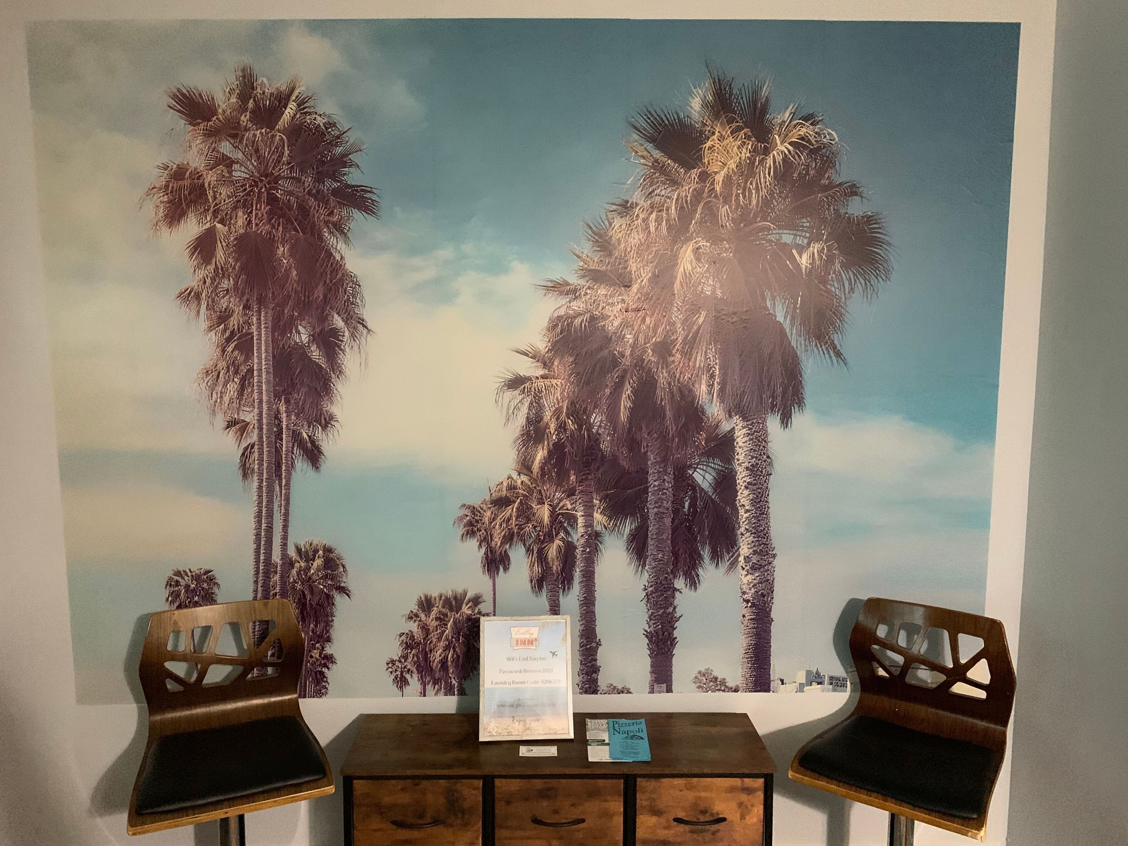 A room with two wooden chairs, a small table, and a wall with a palm tree mural.