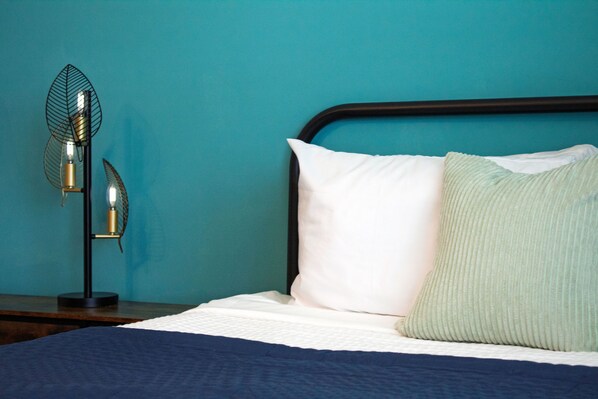 A bedroom detail featuring a black metal bed frame against a vibrant teal wall.
