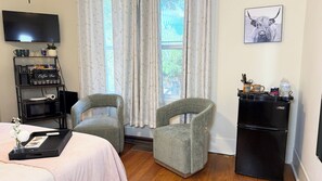 A hotel room with a bed, two armchairs, a coffee bar, a TV, and a refrigerator.
