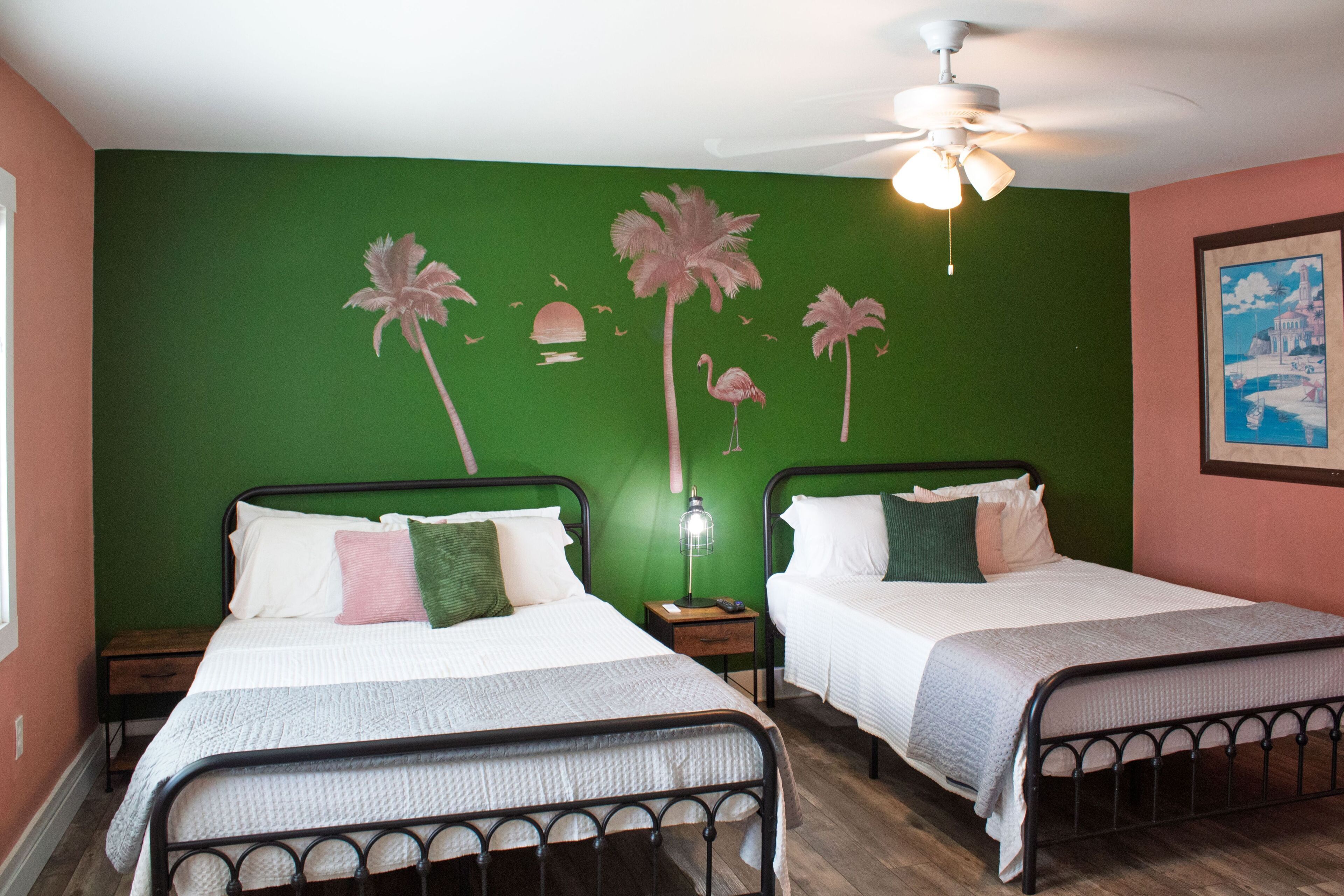Bedroom with two metal-frame beds and a green accent wall with palm tree artwork.