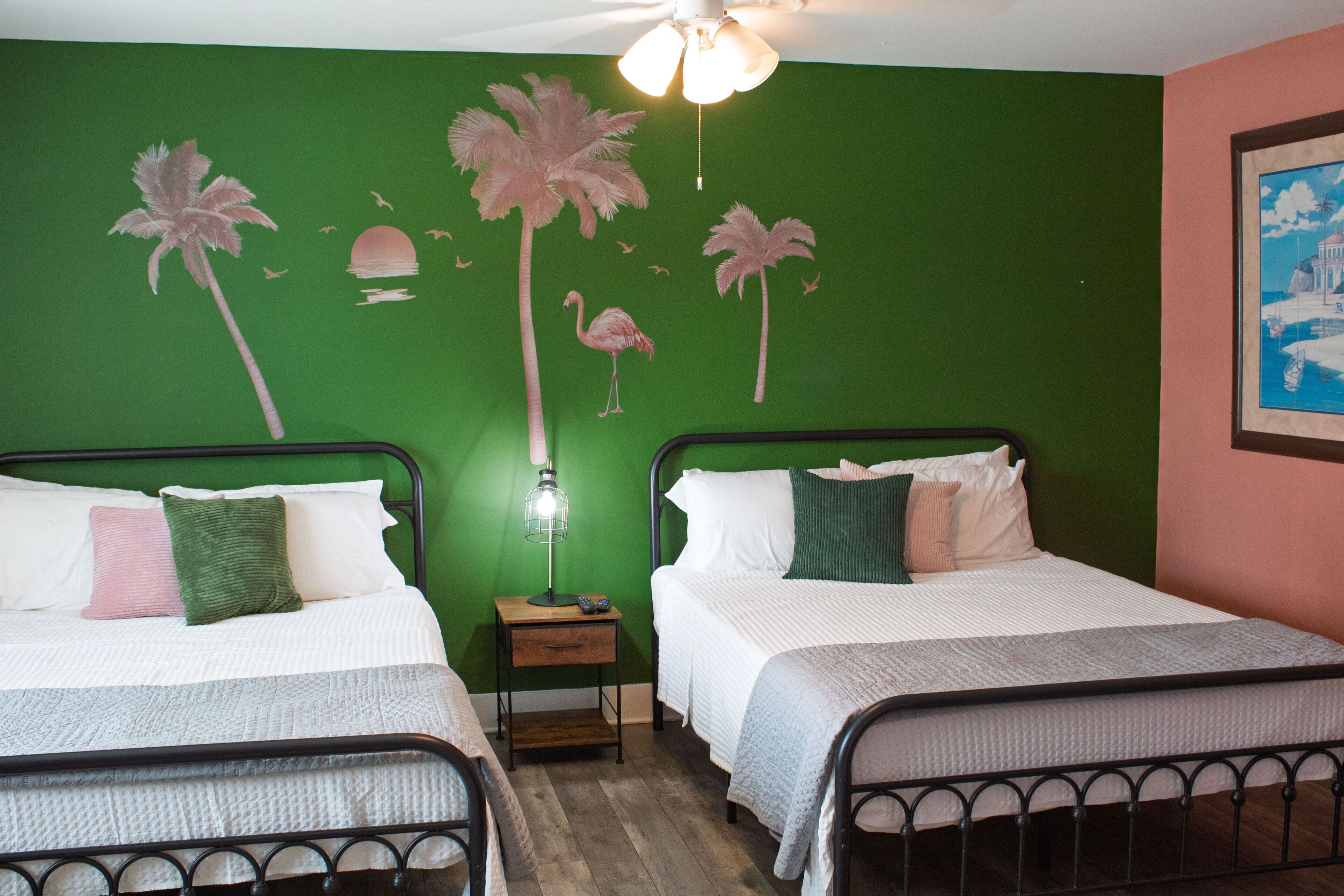 Bedroom with two metal-framed beds against a green tropical-themed accent wall.