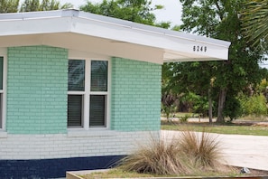 Painted brick exterior corner featuring a projecting flat roofline and landscaping.
