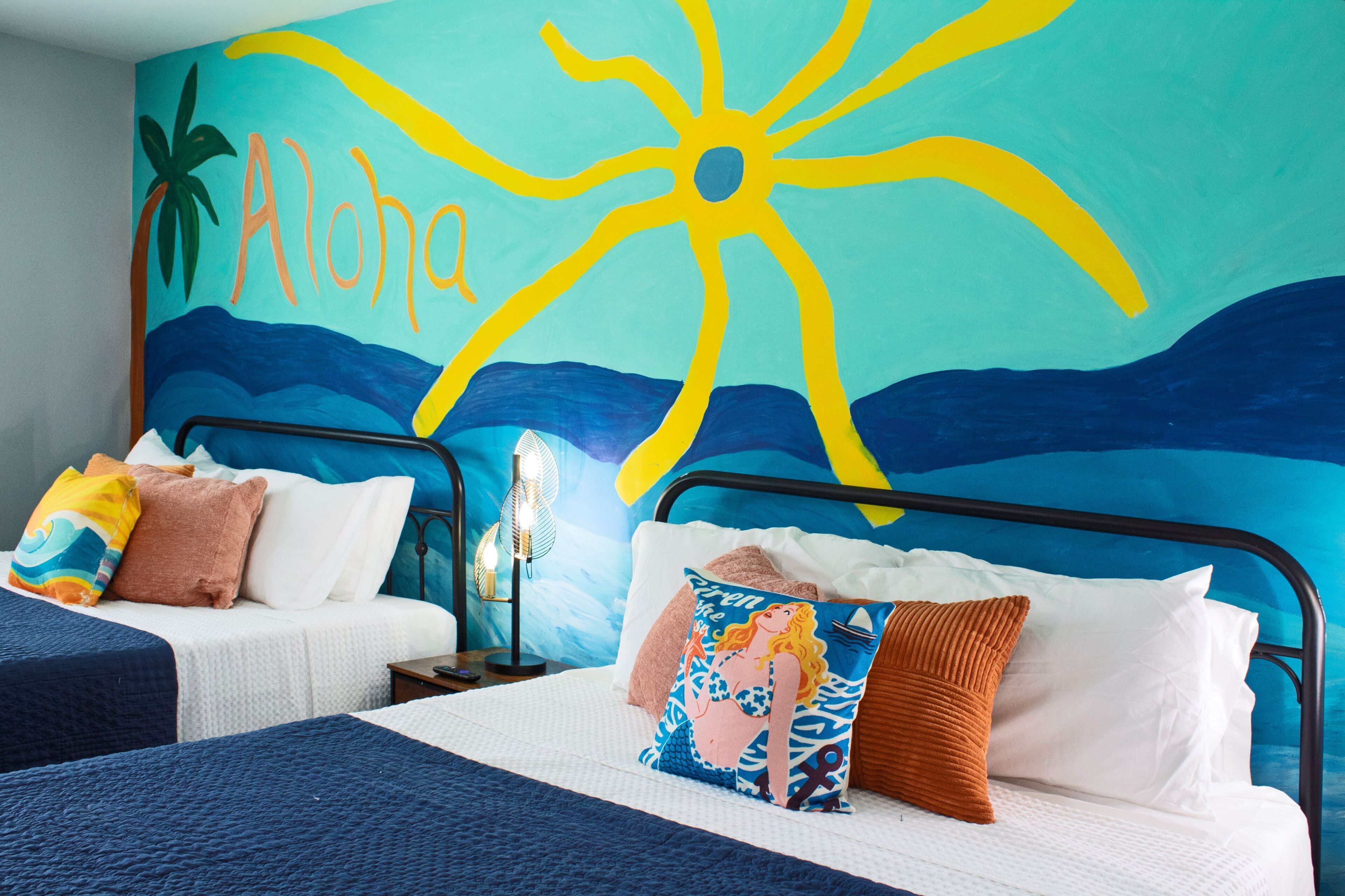 Bedroom with two beds and a colorful tropical mural on the wall.