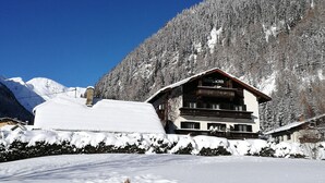 Un chalet enneigé doté d’un balcon, entouré de montagnes et d’arbres.