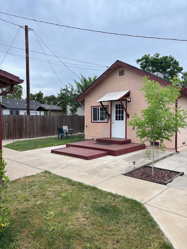 A single-story house with a front porch, a small yard, and a tree.