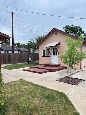 A single-story house with a front porch, a small yard, and a tree.