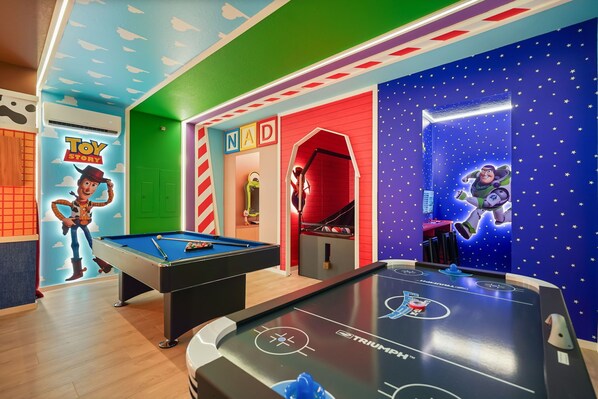 Un espace de jeux pour enfants comprenant une table de billard, une table de baby-foot et une salle décorée sur le thème de « Toy Story ».