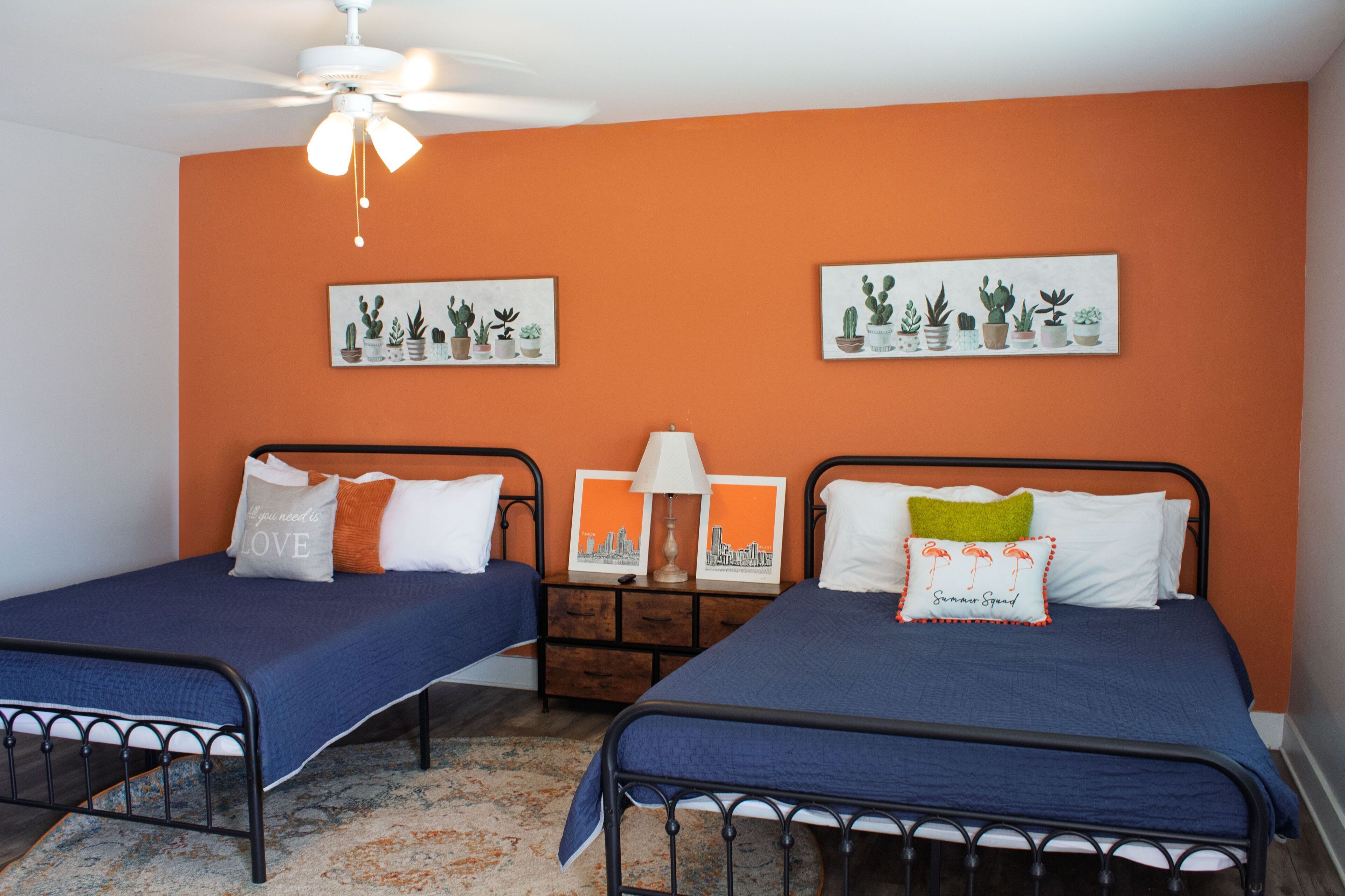 Bedroom with two beds, an orange accent wall, and a ceiling fan.