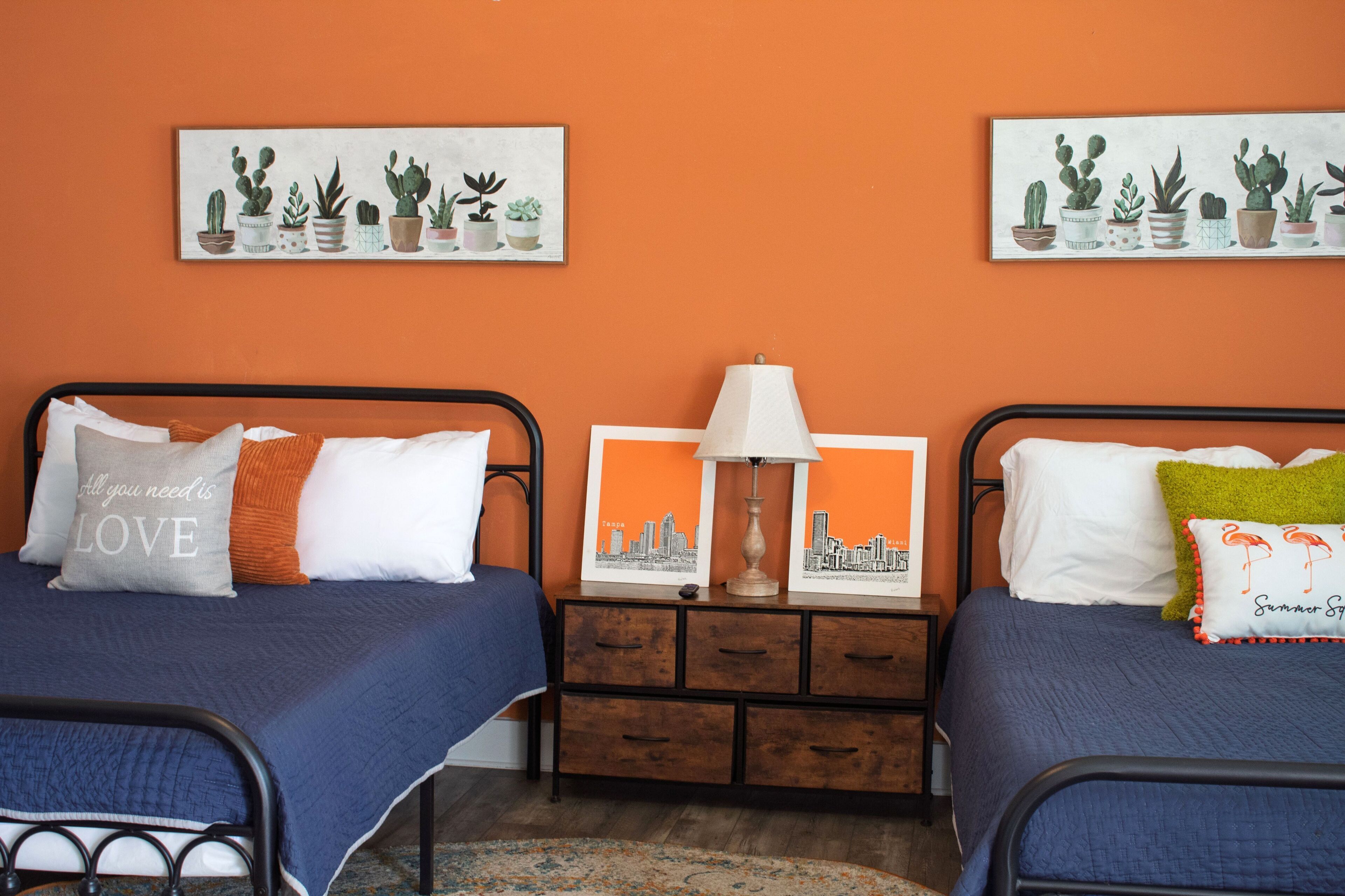 A colorful bedroom setup with two metal beds against an orange accent wall.