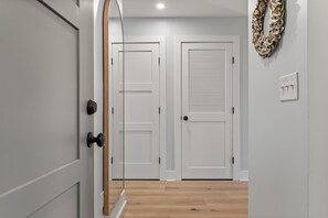 A hallway with two white doors, a light switch, and a wall-mounted decorative item. - Modern, Dog-Friendly Marsh Retreat (Mount Pleasant)