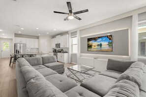 Ein modernes Wohnzimmer mit einem grauen Ecksofa, einem Glastisch und einem Deckenventilator.