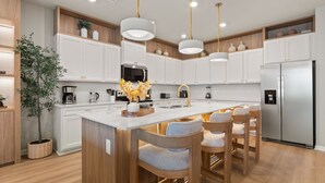 Una cocina moderna con armarios blancos, electrodomésticos de acero inoxidable y una isla central con taburetes de bar.