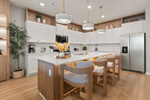 A modern kitchen with white cabinetry, stainless steel appliances, and a central island with bar stools. - 10 BD/ 8 BA/ Windsor Cay (1003 CR) (Clermont)
