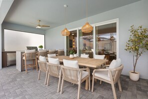 Comedor con mesa de madera, sillas de mimbre, ventilador de techo e iluminación colgante.