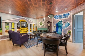 Una habitació amb taula de joc d'escacs, butaques còmodes, un mural d'un personatge de dibuix animat i una paret de maó amb un rètol de Monsters University.