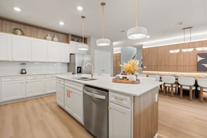 Una cocina moderna con armarios blancos, lavavajillas de acero inoxidable y una isla central con un fregadero y un jarrón de flores.
