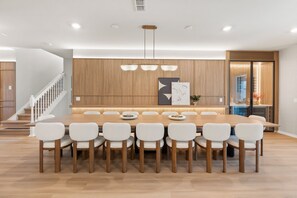 A modern dining area with a wooden table and white chairs, a staircase, and a kitchen visible through an open door. - 10 BD/ 8 BA/ Windsor Cay (1003 CR) (Clermont)