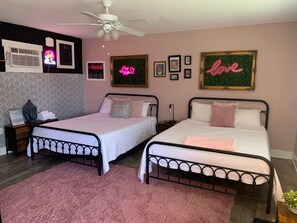 A bedroom with two beds, a ceiling fan, a pink rug, and various wall decorations.