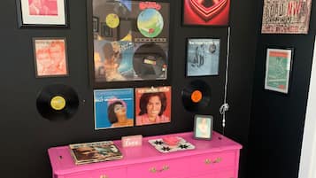 A bright pink vintage console cabinet rests against a black vinyl-themed gallery wall.