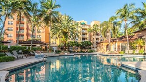 Une piscine entourée de palmiers et un immeuble à plusieurs étages doté de balcons.