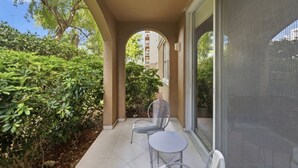 Une terrasse couverte avec deux chaises et une table, entourée de verdure et offrant une vue sur un bâtiment en arrière-plan.