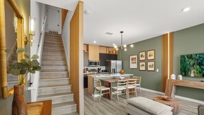 Une cuisine moderne dotée d’un îlot central, d’un escalier en bois et d’un coin repas avec des chaises.