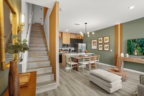 A modern kitchen with a central island, wooden staircase, and a dining area with chairs. - 3 BD/ 3 BA/ The Hub At Westside (3349 TT) (Kissimmee)