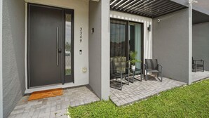 Un bâtiment moderne avec une porte noire, une porte vitrée donnant sur un beau paysage, et une terrasse avec des chaises et une table.