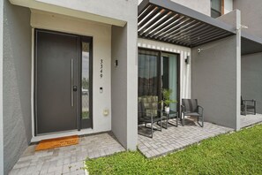 A modern building with a black door, a glass door with a view, and a patio with chairs and a table. - 3 BD/ 3 BA/ The Hub At Westside (3349 TT) (Kissimmee)