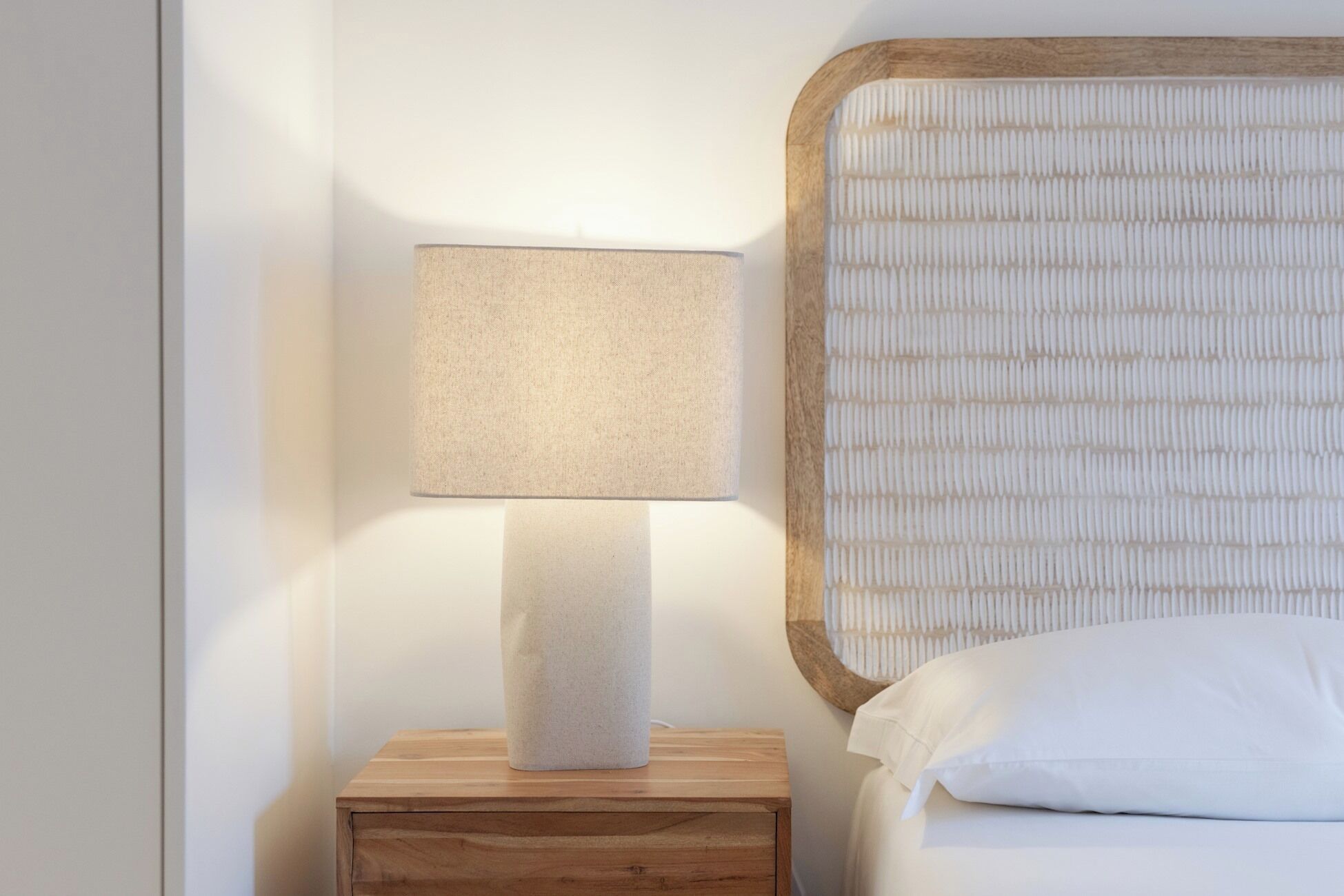 Una cama con cabecera de madera y una mesita de noche con lámpara.
