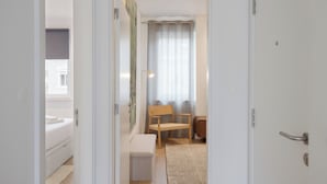 Ett hotellrum med en säng, en stol, ett litet bord och ett fönster med gardiner.