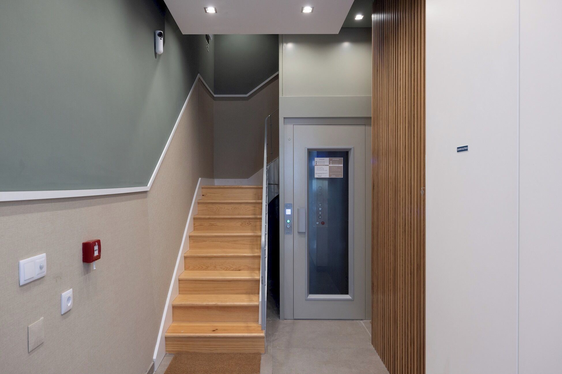 A staircase leading to an elevator with a control panel, a fire alarm, and a door with a sign.