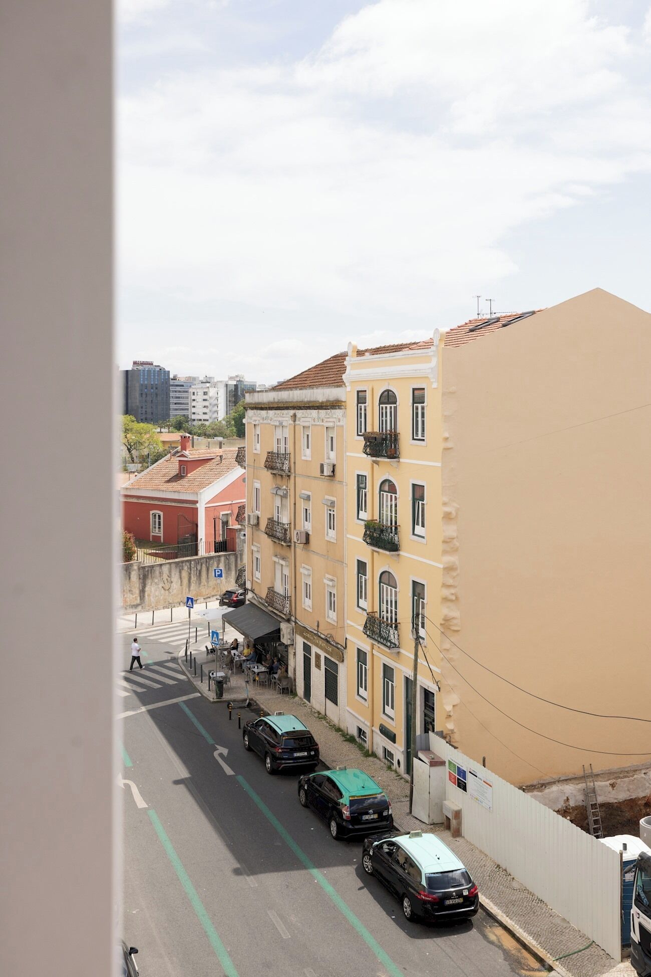 A street view with parked cars, a pedestrian crossing, and buildings with balconies.