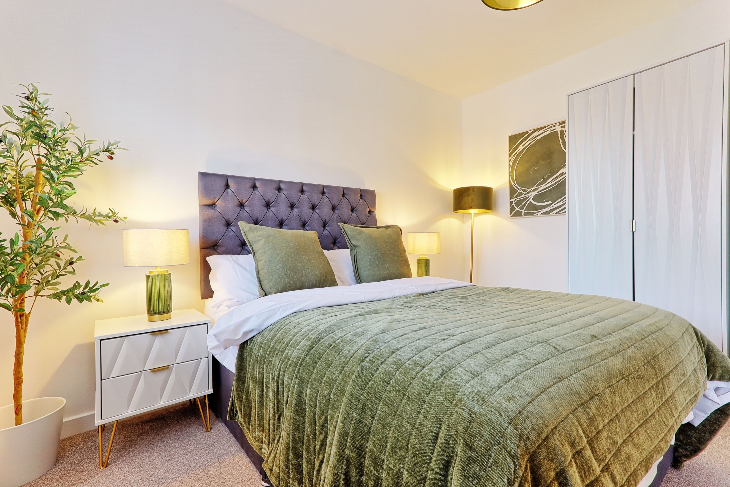 A neatly made bed with a green quilt, a tufted headboard, and two bedside lamps.